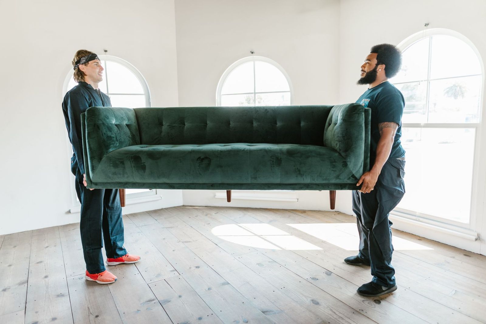 Zwei Männer heben ein grünes Sofa in einem hellen Raum mit Bogenfenstern