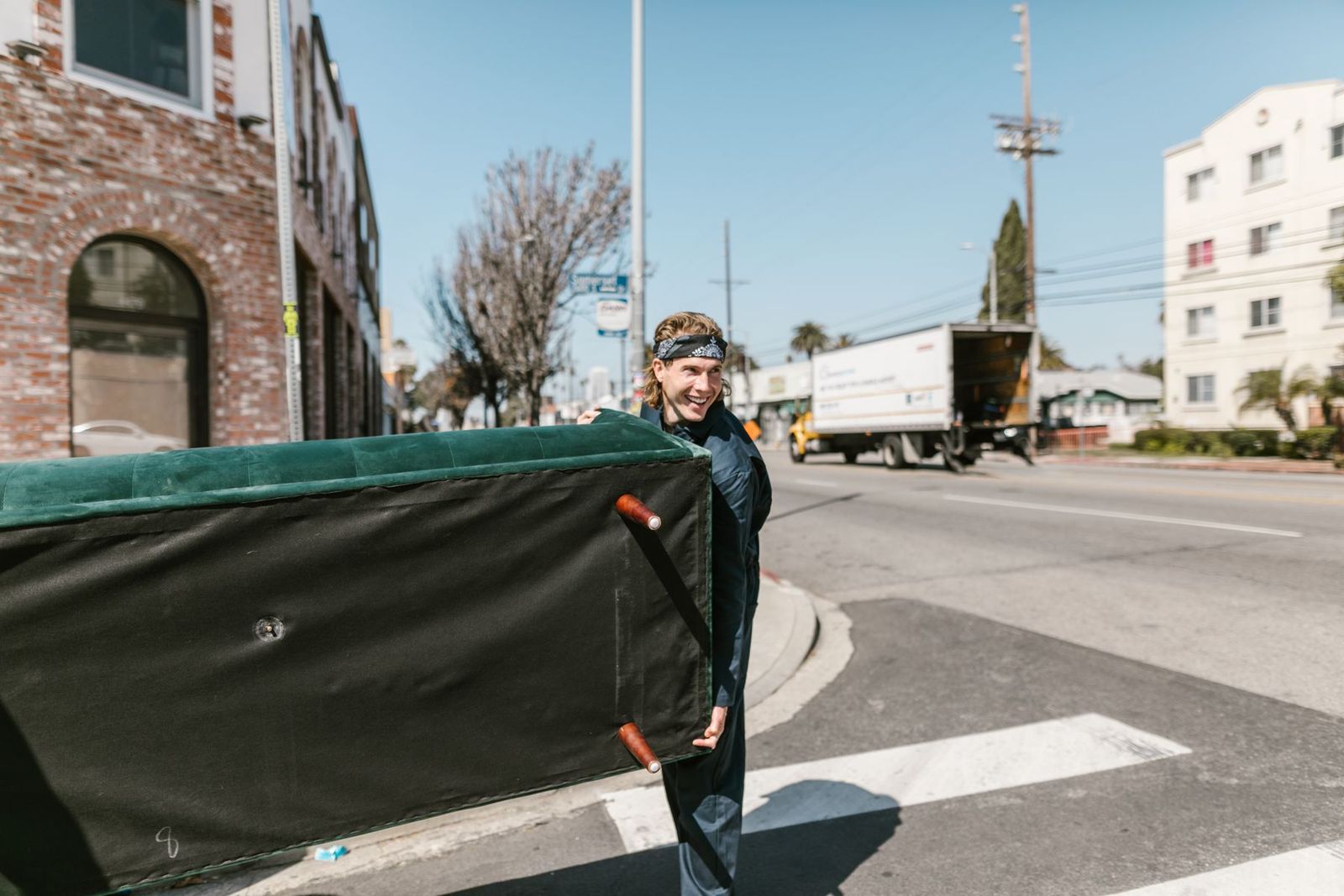 Mann trägt eine große Couch über eine sonnige Straße